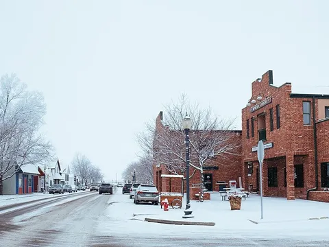 Fifth Street in old-town Frederick at Oak Street under snow in 2018: a two-story red-brick corner building with a stepped parapet, frosted bare trees, a black lamppost and a few cars on the plowed street.